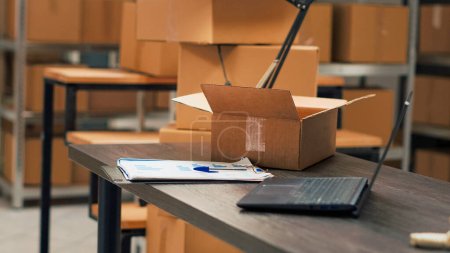 Photo for Storehouse space and desk filled with cardboard boxes and goods, storage shelves with merchandise and products. Warehouse racks used for supply management and shipping logistics. Handheld shot. - Royalty Free Image