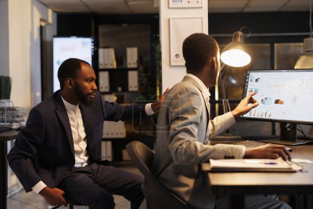 Téléchargez les photos : Des collègues afro-américains analysant la stratégie marketing discutant du rapport de croissance financière, travaillant tard dans la nuit dans le bureau de démarrage de l'entreprise. Planification de l'équipe de direction plan de recherche - en image libre de droit