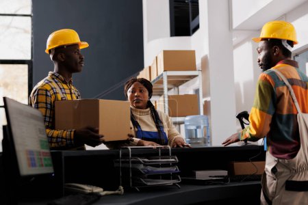 Photo for Postal service workers bringing received parcel for registration at reception desk. African american shipment operators managing package dispatching in delivery company warehouse - Royalty Free Image