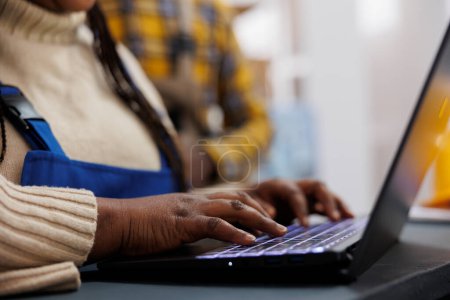 Téléchargez les photos : African American entrepôt travailleur armes écriture sur ordinateur portable et en utilisant l'application d'inventaire des stocks. Entrepôt employé vérifier les produits listant en ligne et tapant sur le clavier de l'ordinateur fermer - en image libre de droit