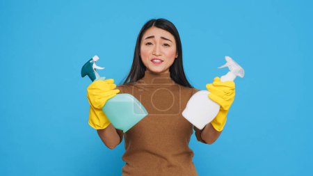 Foto de Cheerful house cleaner wearing yellow rubber gloves while showing chemical detergent spray in front of camera, promoting cleaning product. Professional housekepper worked hard to maintain a clean home - Imagen libre de derechos