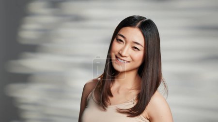 Téléchargez les photos : Young person embracing imperfections for skincare ad, asian model feeling beautiful and posing to promote nourishing beauty routine. Glowing luminous woman with radiant bare skin in studio. - en image libre de droit
