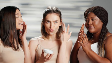 Téléchargez les photos : Femmes interraciales appliquant crème hydratante pour le visage, en utilisant des cosmétiques de soins de la peau pour prévenir les rides sur la caméra. Modèles beauté campagne de publicité pour les produits dermatologiques. routine de soins de la peau. - en image libre de droit