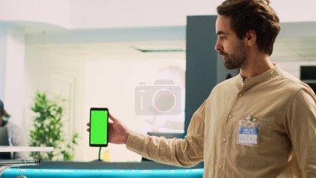 Photo for Man worker holding smartphone with greenscreen, showing blank copyspace template on mobile phone. Caucasian market assistant using isolated chroma key display in clothing store. - Royalty Free Image