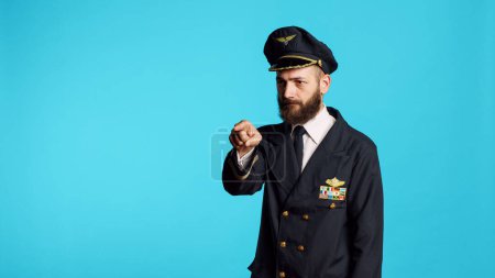 Photo for Plane captain in aviation uniform pointing at camera and choosing, saying i want you for commercial flights aircrew. Young male pilot flying airplane and acting confident, feeling successful. - Royalty Free Image