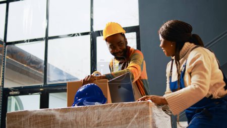 Photo for African american people laughing in depot space, being funny and making jokes together while they pack products in containers. Young employees having fun with quality control. Handheld shot. - Royalty Free Image