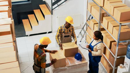 Photo for African american people packing products in boxes before doing quality control to ship merchandise. Warehouse employees checking inventory and stock logistics, retail shipment. Handheld shot. - Royalty Free Image