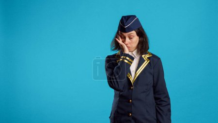 Photo for Air hostess feeling tired and yawning in studio, being drained and worn out after commercial flight work. Aircrew member dressed as stewardess being exhausted and falling asleep. - Royalty Free Image