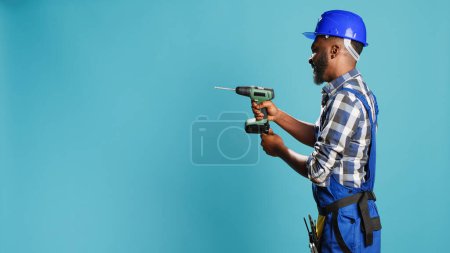 Photo for Male builder using power drill instrument on wall, drilling nails with cordless machine tool on camera. Professional mechanic with hardhat holding nail gun to drill holes, building machinery. - Royalty Free Image