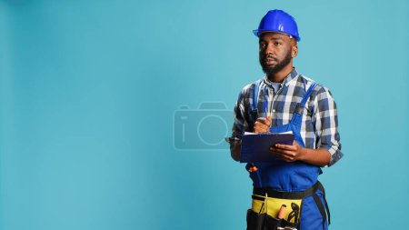 Photo for Young handyman making calculations on files, taking notes on papers before starting new construction building project on camera. Male contractor writing data and measurements. - Royalty Free Image