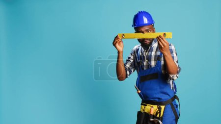 Photo for Young adult measuring surface with bench level tool, checking liquid in water level instrument in studio. Professional mechanic working with aligment equipment, construction balance. - Royalty Free Image