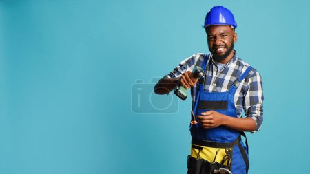 Photo for Young repairman using power drill gun on wall, drilling nails with electronic machine tool in studio. Construction engineer with helmet holding nail gun to drill holes, renovation instrument. - Royalty Free Image