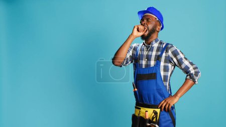 Photo for Male builder yawning on camera feeling worn out, man dressed in overalls and hardhat falling asleep in studio. Tired handyman feeling exhausted and drained after construction project. - Royalty Free Image