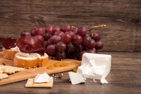 Foto de Jamón, galletas saladas, uva y queso blanco sobre fondo de madera en foto de estudio - Imagen libre de derechos
