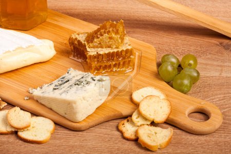 Téléchargez les photos : Délicieuse assiette de fromage avec craquelins, miel et raisin sur fond de bois - en image libre de droit
