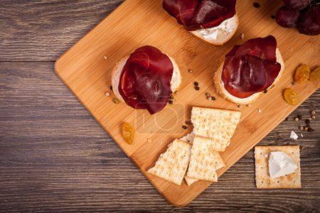 Photo for Top view of plate with ham, crackers and grape on wooden background in studio photo - Royalty Free Image