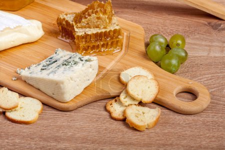 Téléchargez les photos : Miel, fromage blanc et autres fromages avec du raisin sur fond de bois. Nourriture épicerie fine - en image libre de droit