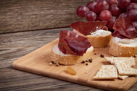 Téléchargez les photos : Combinaison saine d'aliments à base de prosciutto, de raisins et de pain sur fond de bois - en image libre de droit