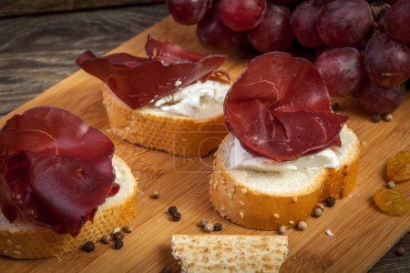 Photo for Italian sliced prosciutto on bread and grapes in the back on wooden table in studio photo - Royalty Free Image