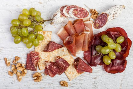 Téléchargez les photos : Photo du jambon italien, des craquelins et du raisin sur fond vintage en bois blanc. Luxe mode de vie sain - en image libre de droit