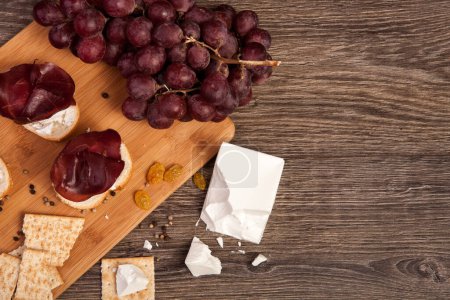 Photo for Ham, crackers, grape and white cheese on wooden background in studio photo - Royalty Free Image