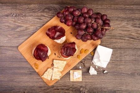 Téléchargez les photos : Jambon, craquelins, raisin et fromage blanc sur fond bois en studio photo - en image libre de droit