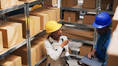 Photo for Team of employees checking stock on laptop and tablet, using devices to plan goods logistics in warehouse area. Young people working with cardboard packages and cargo products. Tripod shot. - Royalty Free Image