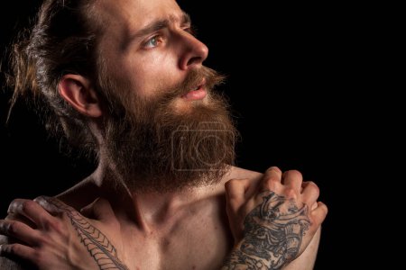 Foto de Retrato de tipo hipster barbudo tatuado sobre fondo negro en foto de estudio. Expresión y moda - Imagen libre de derechos