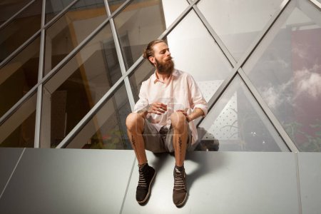 Photo for Cool bearded tattooed guy posing in front of office building. Modern start up company - Royalty Free Image
