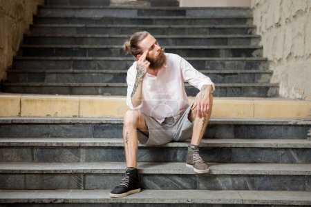 Téléchargez les photos : Élégant tatoué et barbu guy posant en plein air dans la ville - en image libre de droit