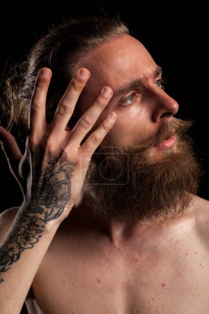 Foto de Retrato de tipo barbudo tatuado fresco sobre fondo negro en foto de estudio. Expresión y moda - Imagen libre de derechos