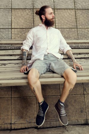 Téléchargez les photos : Beardead tatoué cool regarder gars assis sur une chaise et regardant loin de la caméra - en image libre de droit