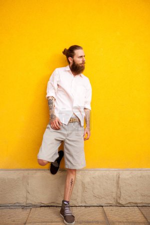 Photo for Tattooed bearded attractive man on yellow wall posing outdoor - Royalty Free Image