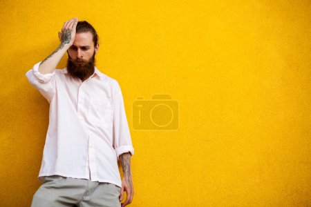 Téléchargez les photos : Cool hipster barbu sur mur jaune posant en plein air - en image libre de droit
