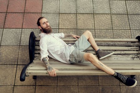 Photo for Bearded tattooed lying on chair and posing in fashion style. Nonconformism and hipster - Royalty Free Image