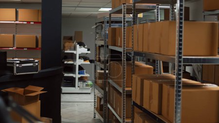 Foto de Storage room area in warehouse with carton packages, office with laptop and industrial products, working on stock logistics and distribution. Small business space with stacks of boxes. - Imagen libre de derechos