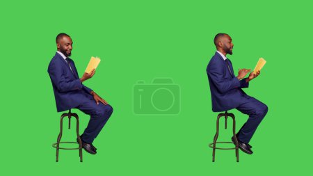 Téléchargez les photos : Jeune homme d'affaires assis sur une chaise à lire un livre d'histoire ou un roman, se concentrant sur le conte fictif pour les loisirs. Entrepreneur confiant lisant la littérature sur plein écran vert du corps. - en image libre de droit