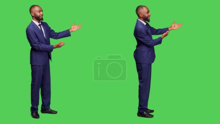 Photo for Young businessman creating presentation in studio, talking about something on left or right sides. Male office employee doing advertisement over full body green screen background. - Royalty Free Image