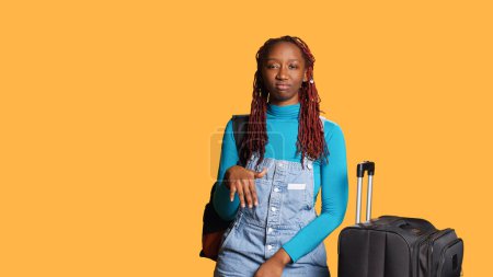 Photo for African american girl nodding head saying no on camera, expressing negative gesture and disapproval. Female tourist with trolley bags for vacation trip, showing rejection and denial. - Royalty Free Image