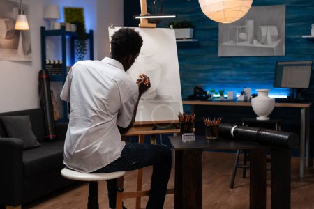 Photo for Master of fine arts making artwork in pencil on canvas easel, sitting in modern art studio. Young african american man with drawing abilities working on outline with creative tools at sketching - Royalty Free Image