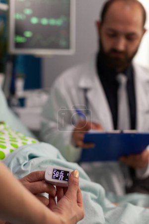 Téléchargez les photos : Infirmière mesurant le taux d'oxygène sanguin avec oxymètre sur un patient âgé couché dans un lit d'hôpital. Homme médecin examinant les résultats des examens médicaux de la femme retraitée, soins spécialisés. - en image libre de droit