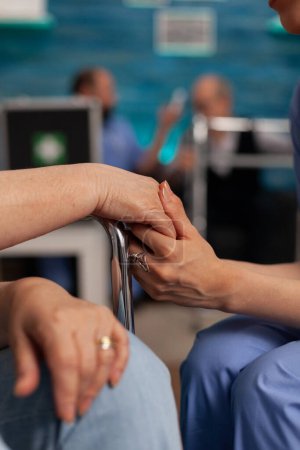Photo for Nurse holding hand of an elderly patient in wheelchair, giving support and motivation in difficult moments. Professional nurses specialized in nursing home care for seniors. - Royalty Free Image