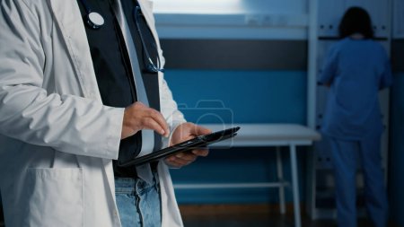 Photo for Close up of practitioner medic holding tablet computer searching for patient illness expertise before start planning health care treatment in hospital office. Medical team working late at night - Royalty Free Image