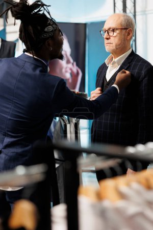 Photo for African american employee helping stylish man with suit in clothing store, client looking to buy modern clothes. Senior customer buying fashionable merchandise and trendy accessories in showroom - Royalty Free Image