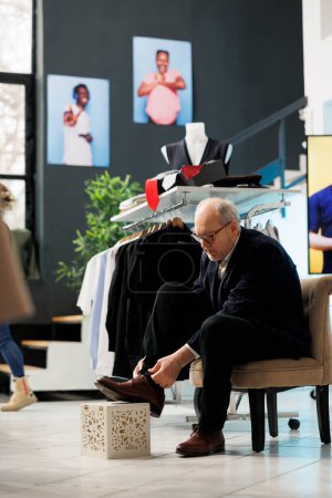 Photo for Senior customer trying elegant shoes in modern boutique, shopping for fashionable clothes and accessories. Elderly stylish man buying new collection in clothing store. Fashion concept - Royalty Free Image
