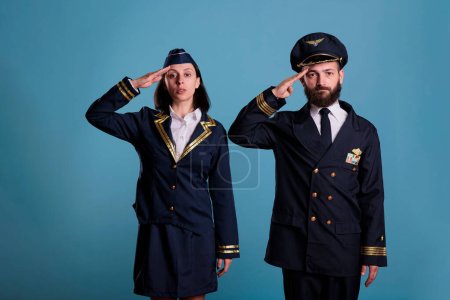 Photo for Airplane pilot and flight attendant saluting portrait, airplane crew in professional uniform. Confident plane captain and air hostess, front view studio medium shot on blue background - Royalty Free Image