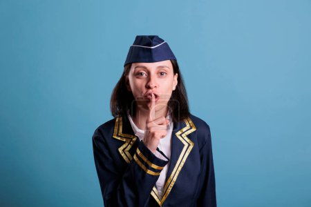 Photo for Flight attendant showing silent gesture, looking at camera with forefinger on lips. Stewardess keeping secret, air hostess whispering front view medium shot, quiet, silence sign - Royalty Free Image