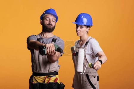 Photo for Builders posing with construction or renovation tools on camera, preparing to do refurbishment project. Construction workers holding roller paintbrush and power drilling gun in studio. - Royalty Free Image