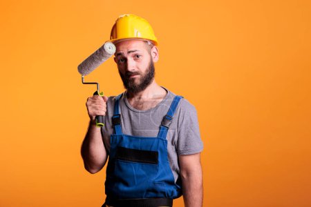 Photo for Professional painter working on renovation with roller, painting walls with color and paintbrush. Construction worker holding rolling brush to do diy renovating project over studio background. - Royalty Free Image