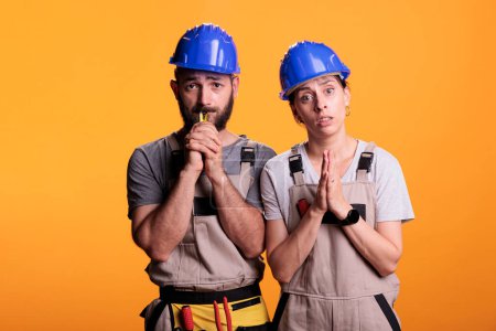 Photo for Construction workers doing prayer hands on camera, begging and wishing for luck or fortune. Team of contractors praying, spiritual faithful builders standing over yellow background. - Royalty Free Image